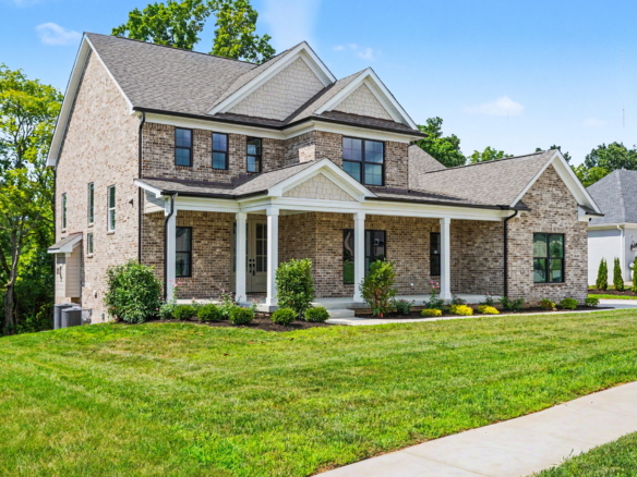 Two-story brick suburban home with a covered front porch, gabled roof, and manicured lawn.