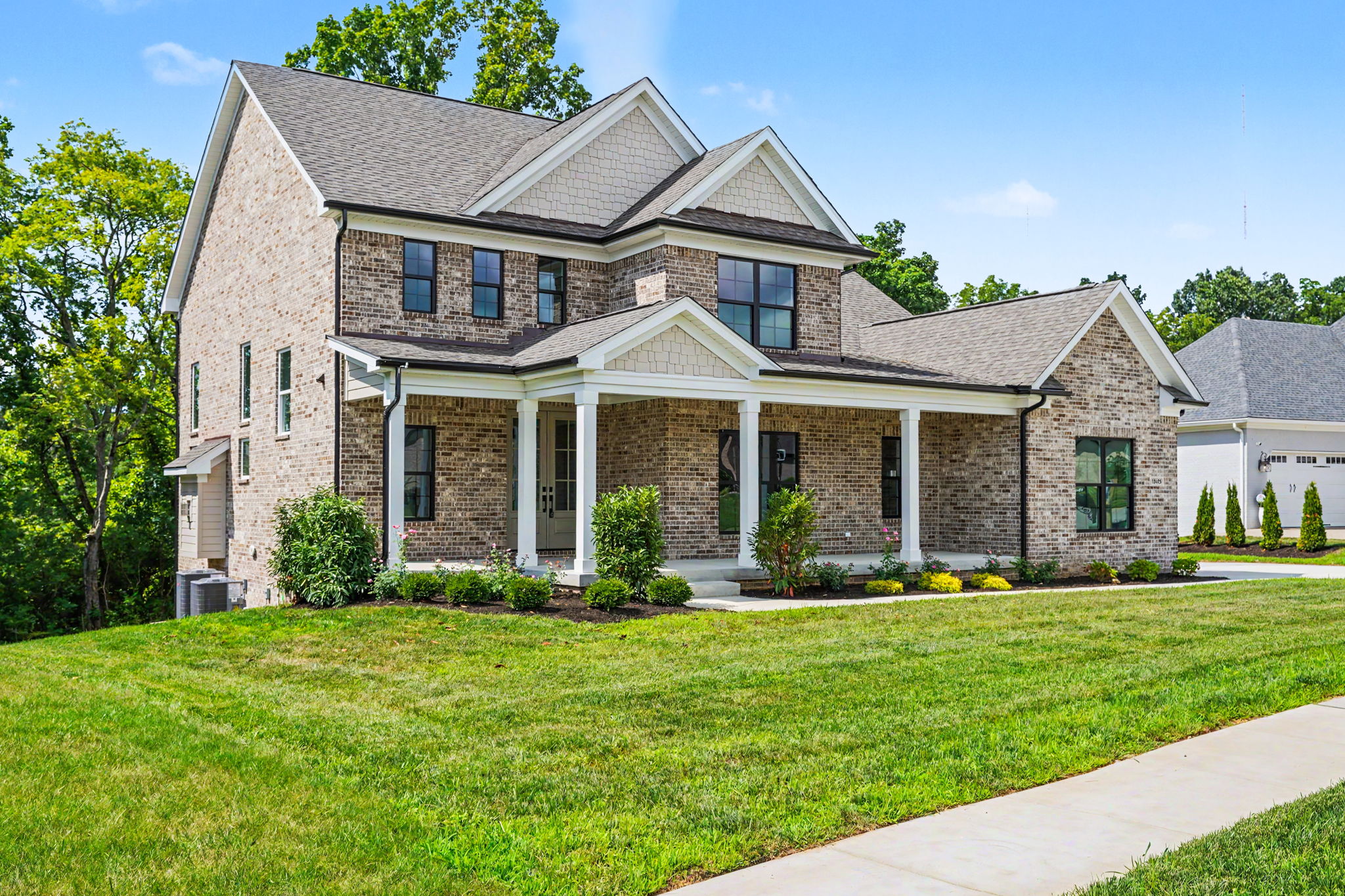 Two-story brick suburban home with a covered front porch, gabled roof, and manicured lawn.