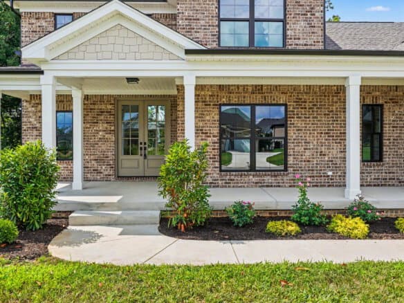 Front porch of a brick home with white columns and landscaping.