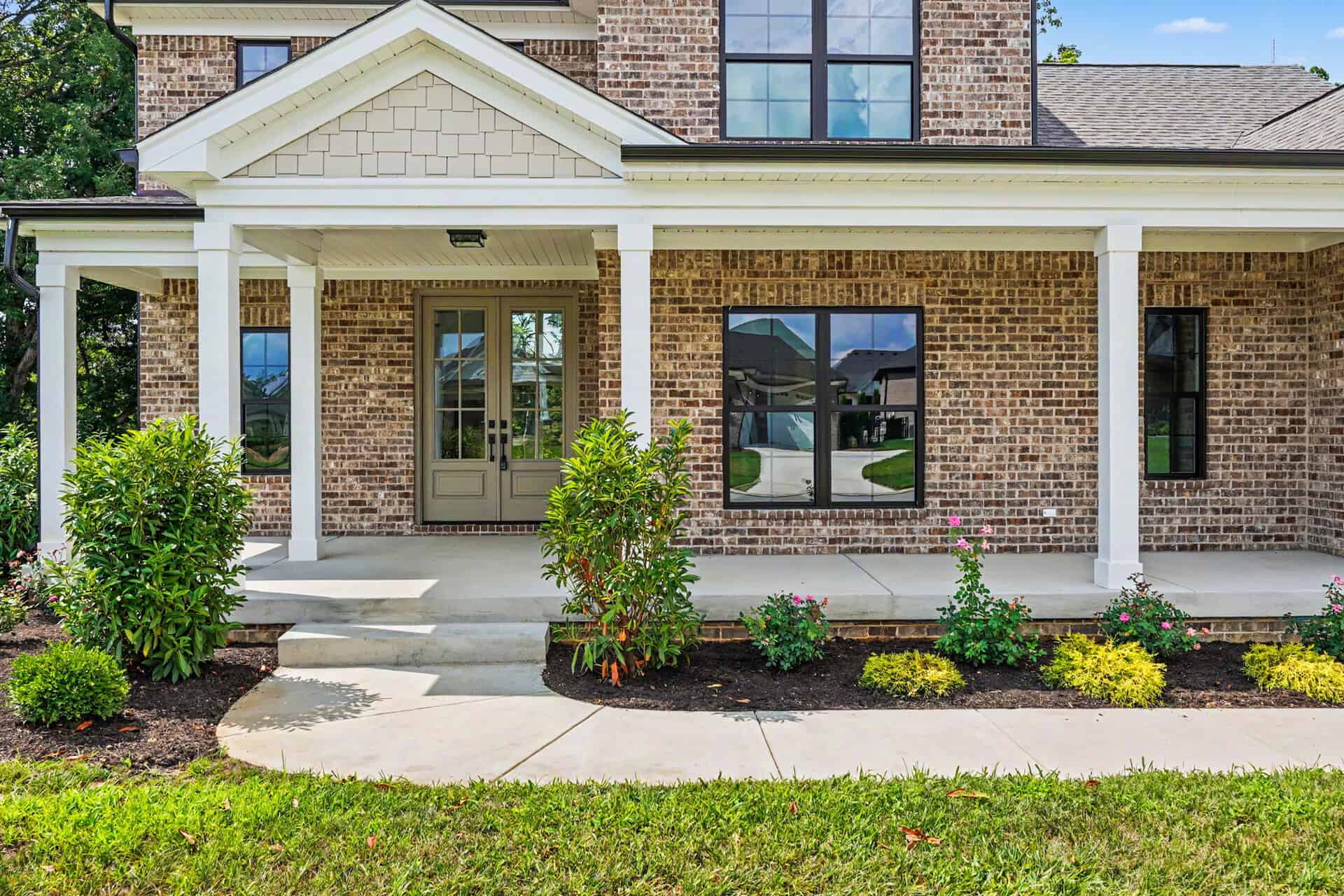 Front porch of a brick home with white columns and landscaping.