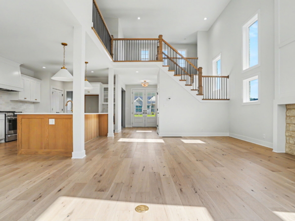 Bright open-concept living space featuring a white kitchen to the left, a central island, and a wooden staircase with black balusters leading to the second floor.