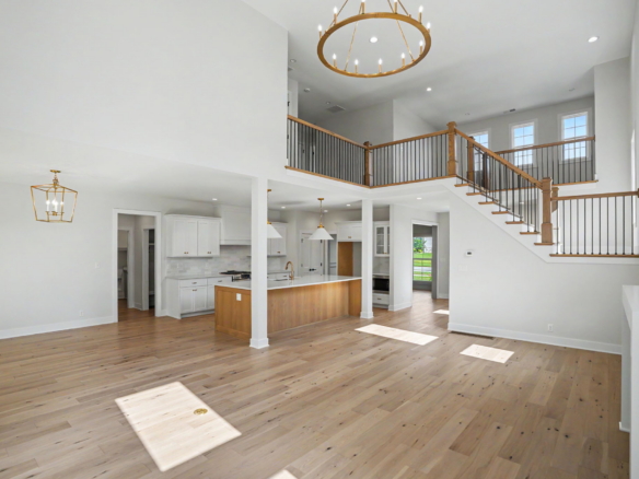 Bright, two-story open-plan living area with white walls, a wooden staircase with black balusters, and a gold circular chandelier.