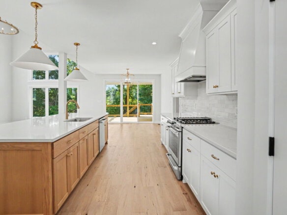 Modern kitchen with white cabinets, island, and large windows overlooking greenery.