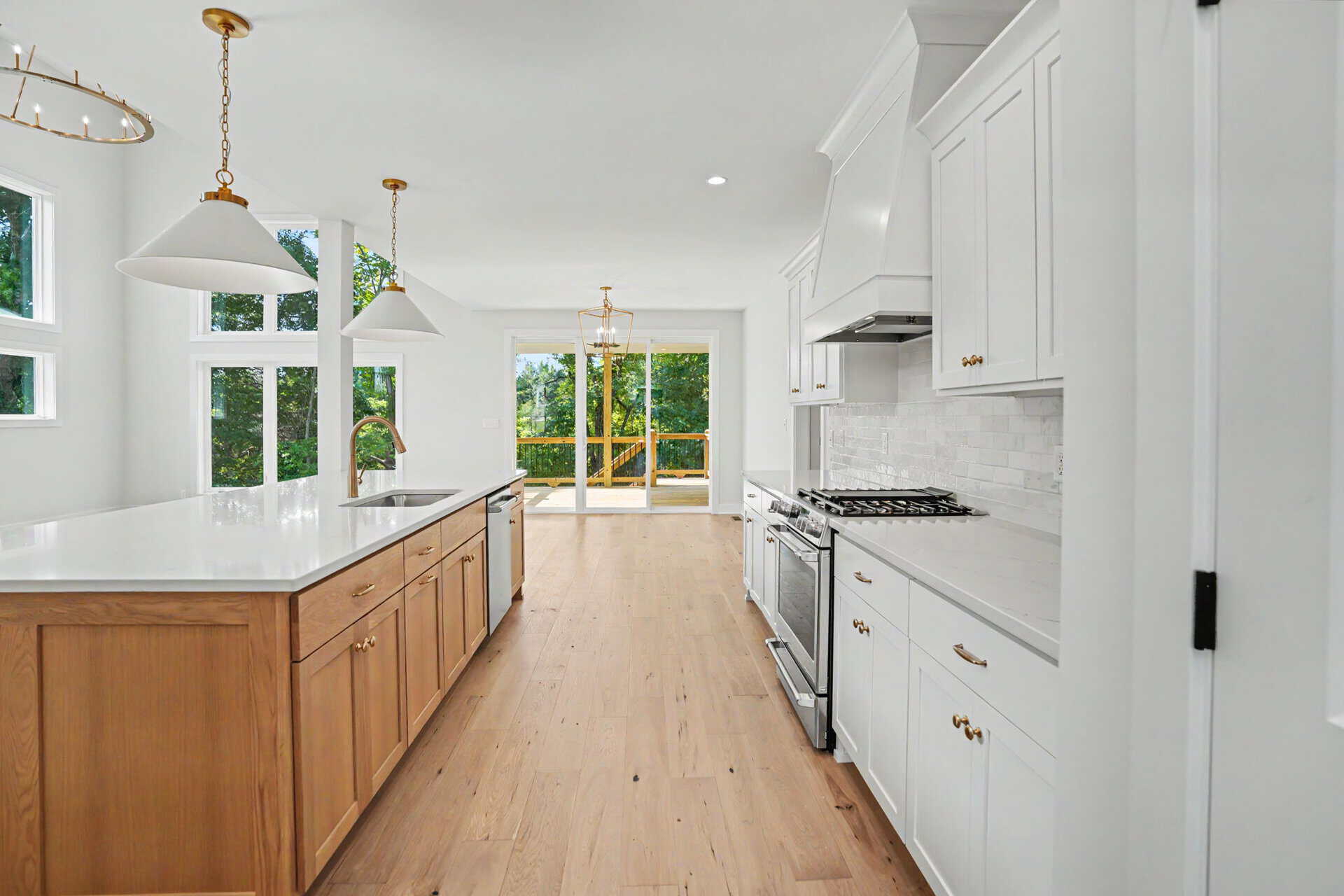Modern kitchen with white cabinets, island, and large windows overlooking greenery.
