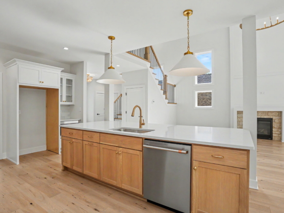 Bright open-concept kitchen with white cabinets, wood island, and two brass pendant lights over a large white countertop island