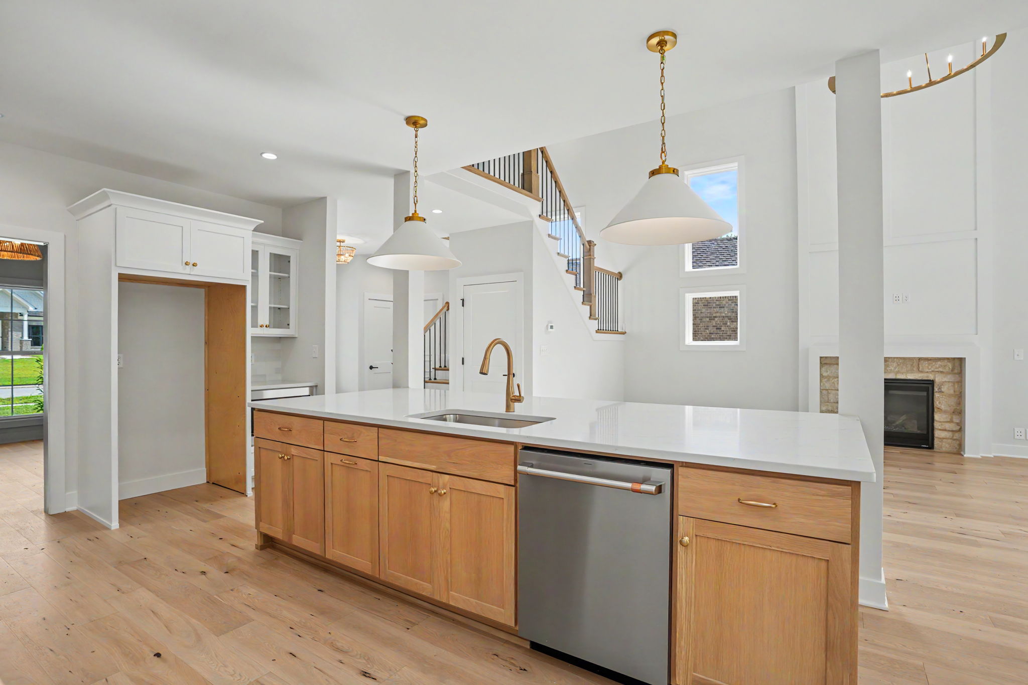 Bright open-concept kitchen with white cabinets, wood island, and two brass pendant lights over a large white countertop island
