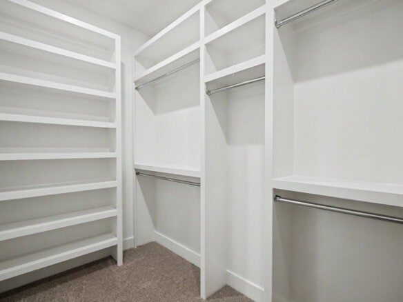 Spacious walk-in closet with white shelving and hanging rods in a new home.