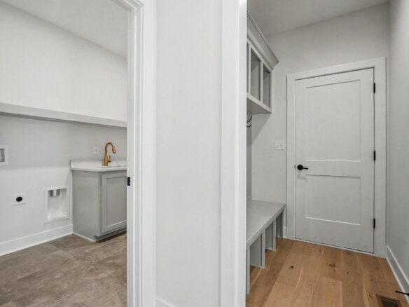 Modern laundry room with white cabinetry and a wooden bench.
