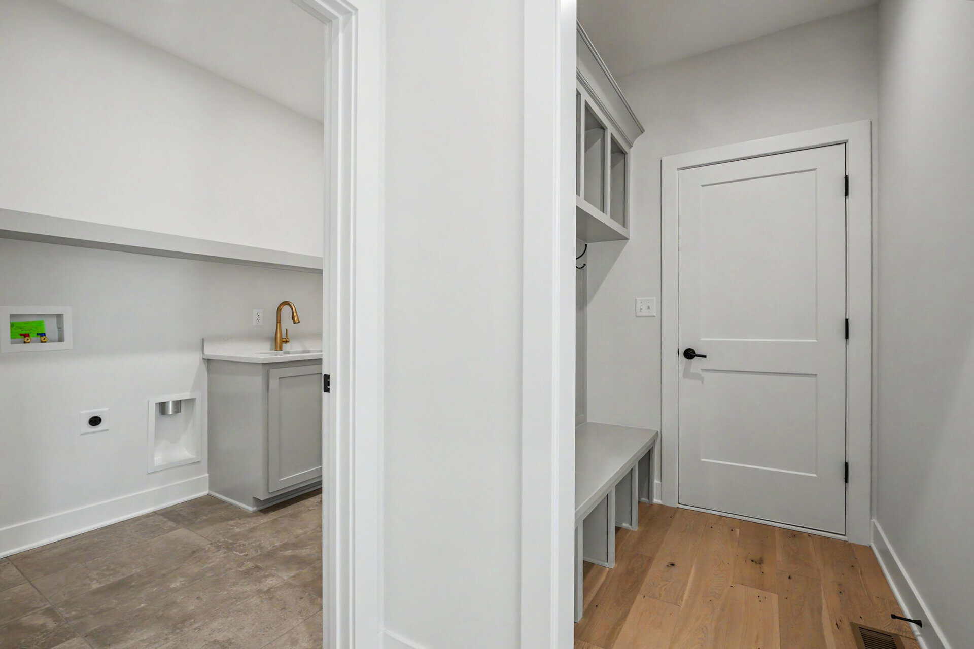 Modern laundry room with white cabinetry and a wooden bench.