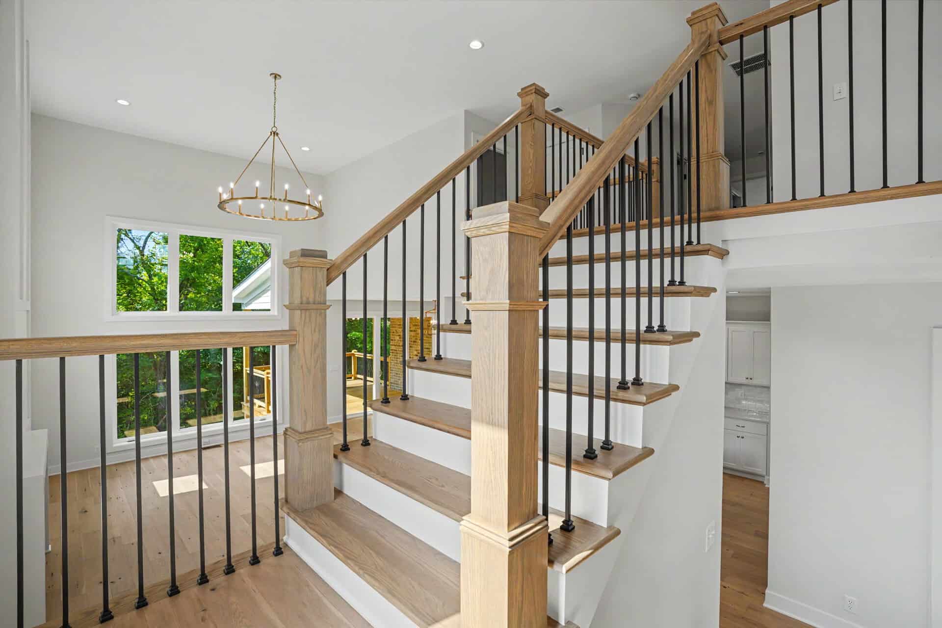 Modern staircase with wooden handrails and black metal balusters in a bright home.