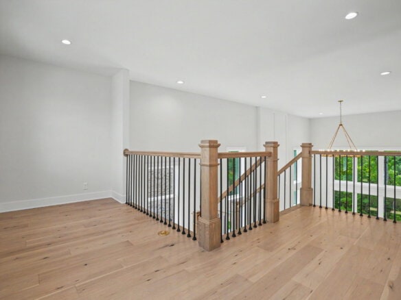 Bright open second-floor landing with wooden railing and large window view.