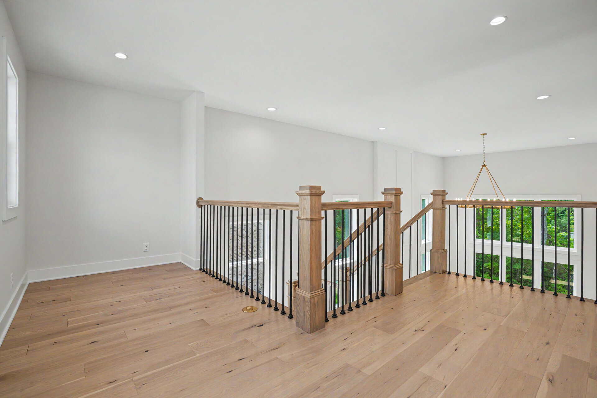 Bright open second-floor landing with wooden railing and large window view.
