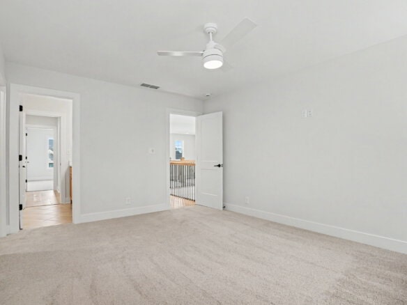 Bright, empty bedroom with white walls, ceiling fan, and beige carpet.