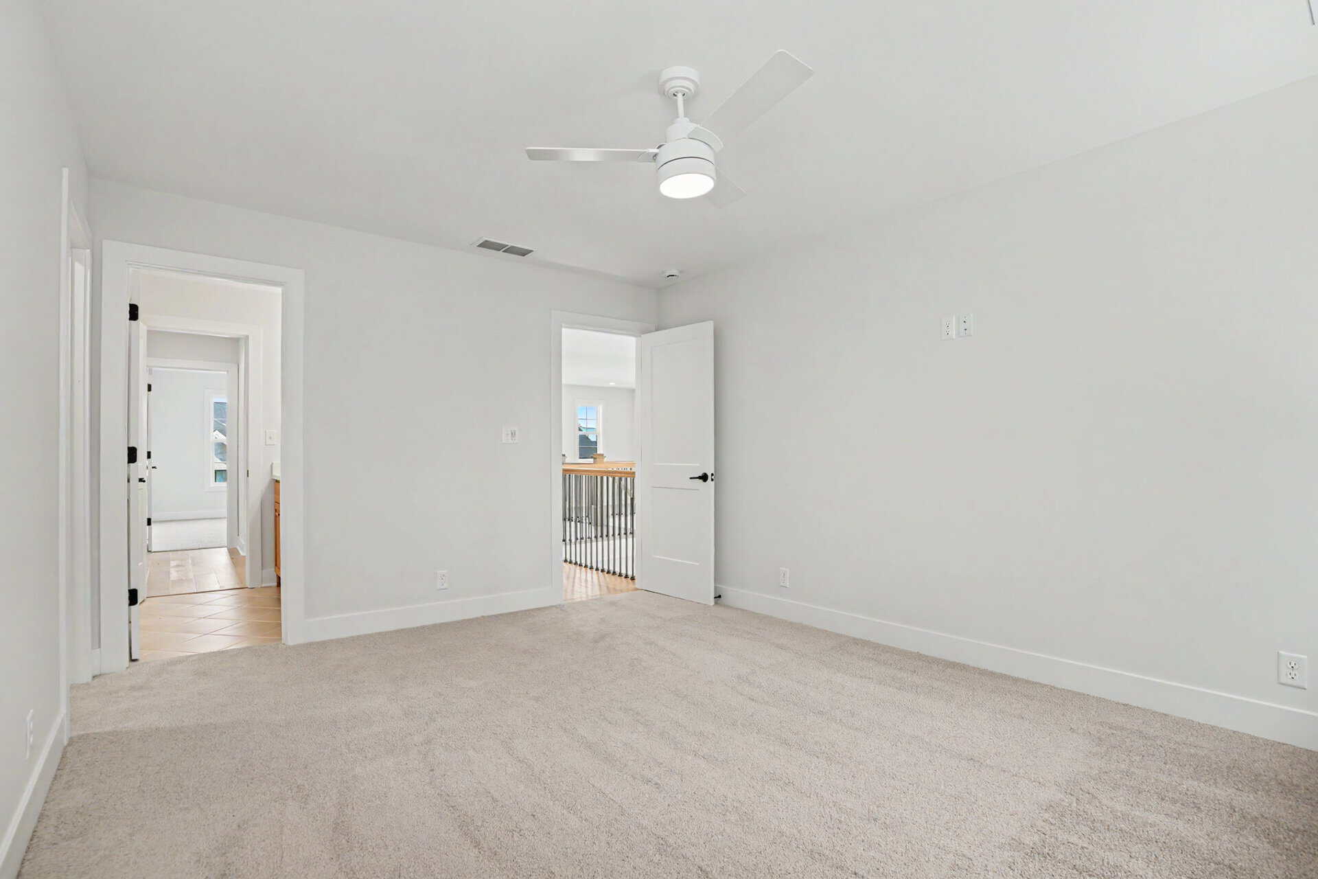 Bright, empty bedroom with white walls, ceiling fan, and beige carpet.