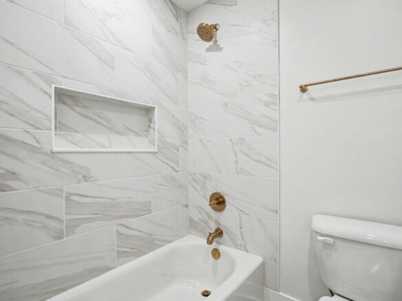 Modern bathroom with marble tiles, bathtub, and gold fixtures.