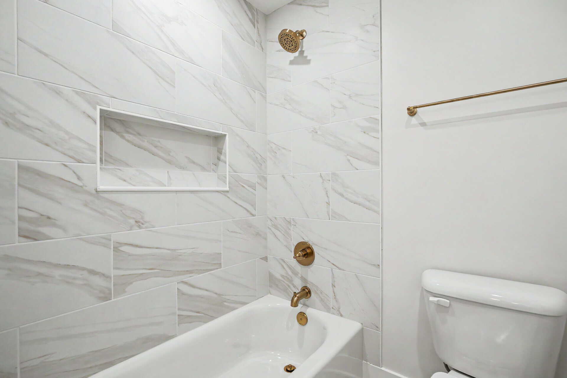 Modern bathroom with marble tiles, bathtub, and gold fixtures.