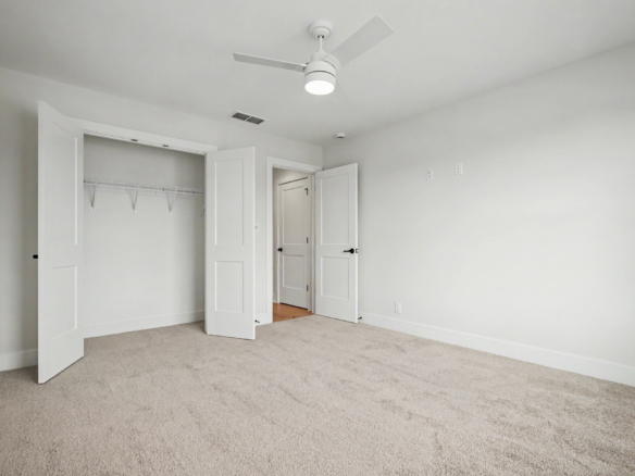 Empty white bedroom with an open closet, two doors, and a ceiling fan overhead.