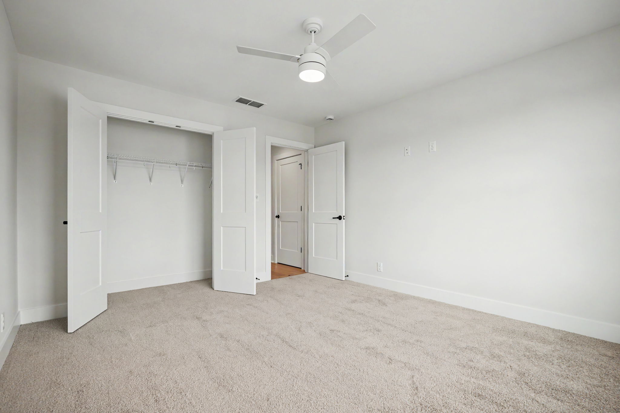 Empty white bedroom with an open closet, two doors, and a ceiling fan overhead.