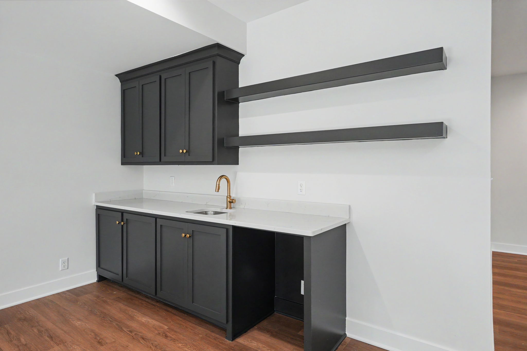Kitchen with dark gray cabinetry, white countertop, and a gold-toned faucet; two long dark metal wall brackets extend from the upper cabinet area.