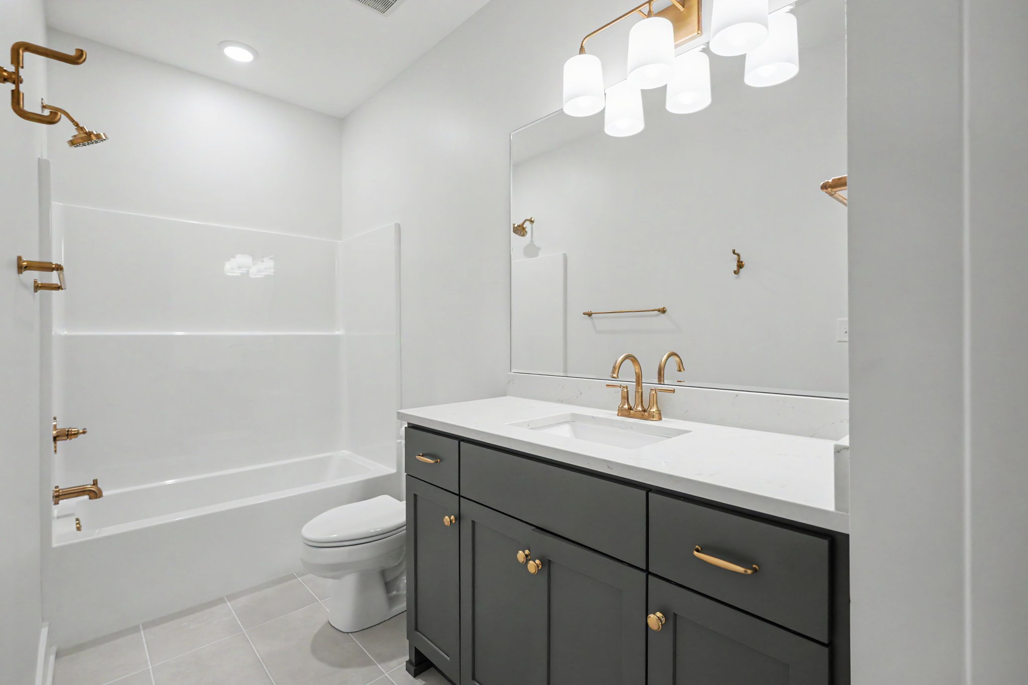 Modern bathroom with a white bathtub, glass shower, and gray vanity topped with white marble; gold fixtures and a large mirror.