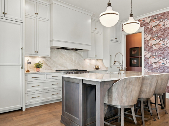 Bright kitchen interior with white cabinets, marble backsplash, and a dark wooden island with seating at the counter edge.