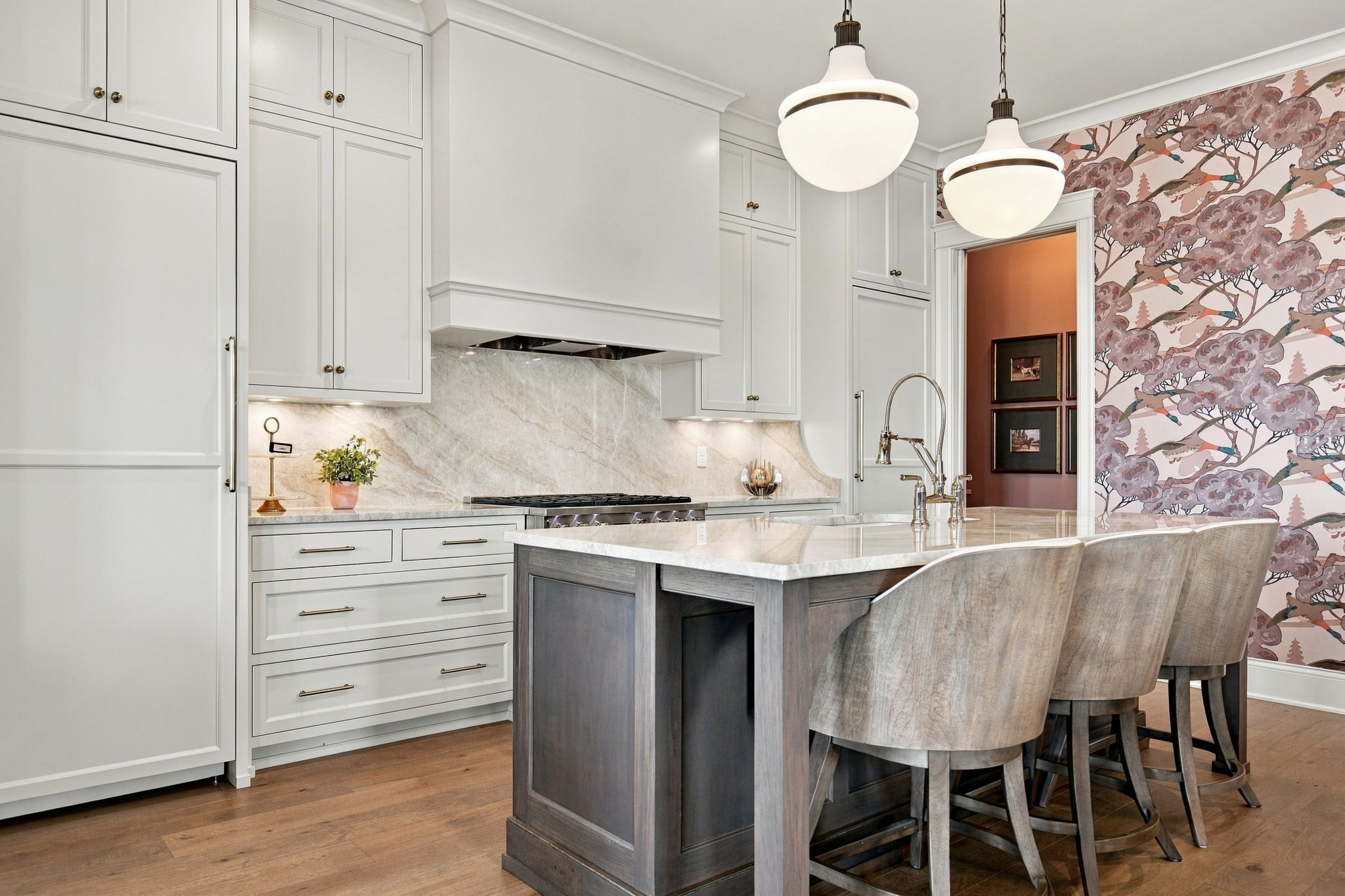 Bright kitchen interior with white cabinets, marble backsplash, and a dark wooden island with seating at the counter edge.