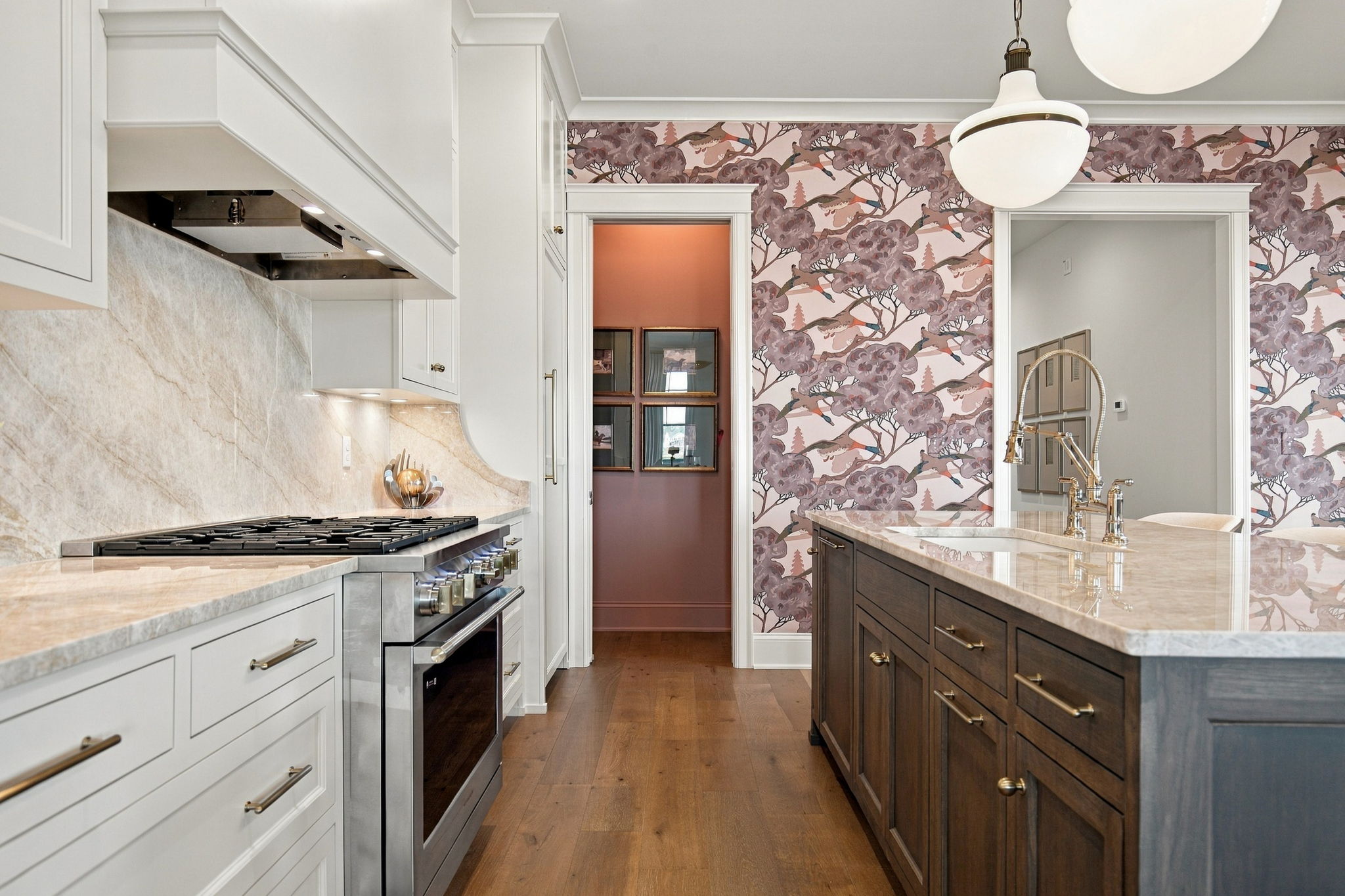 Bright kitchen with white cabinetry, marble countertops, and a dark wood island beside a pink floral wallpapered wall.