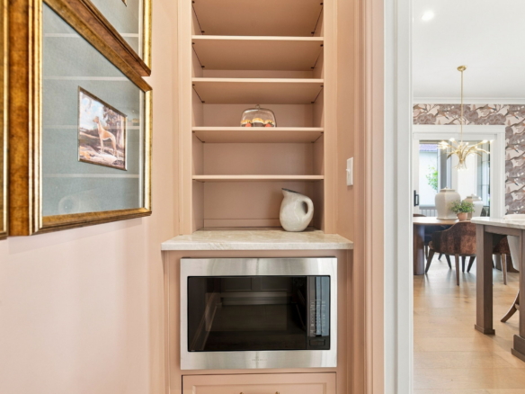 Built-in kitchen shelf with a glass cake dome and a ceramic pitcher beneath, next to a pink cabinet and oven.
