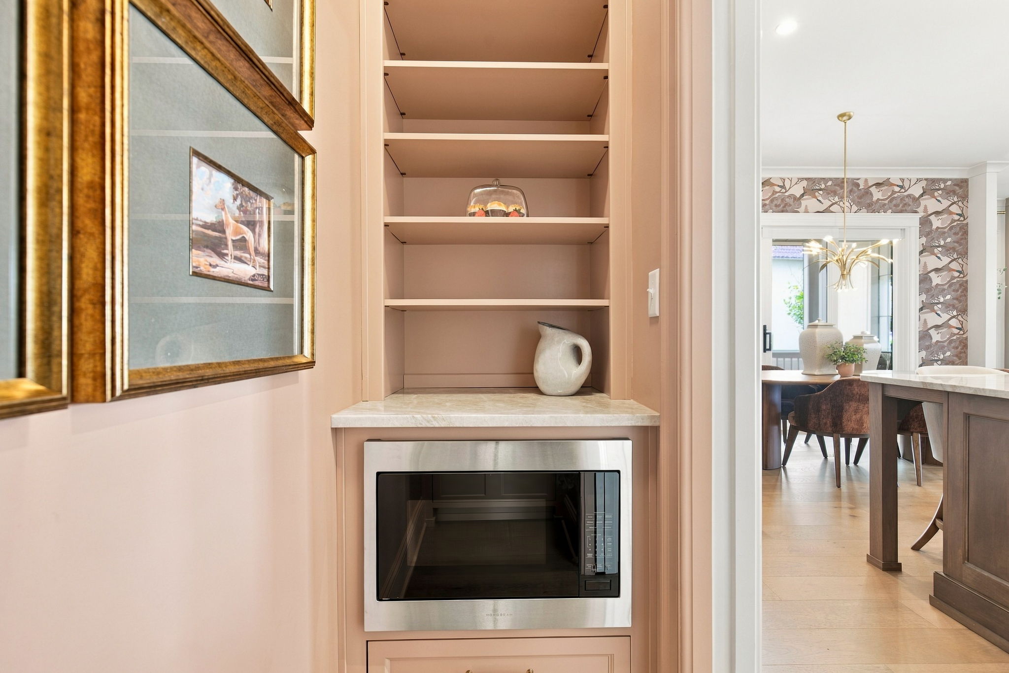 Built-in kitchen shelf with a glass cake dome and a ceramic pitcher beneath, next to a pink cabinet and oven.