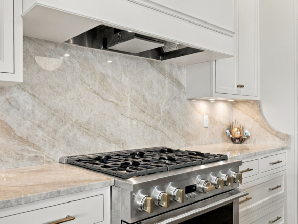 Stainless steel gas range with multiple burners, white cabinetry, and a beige marble backsplash.