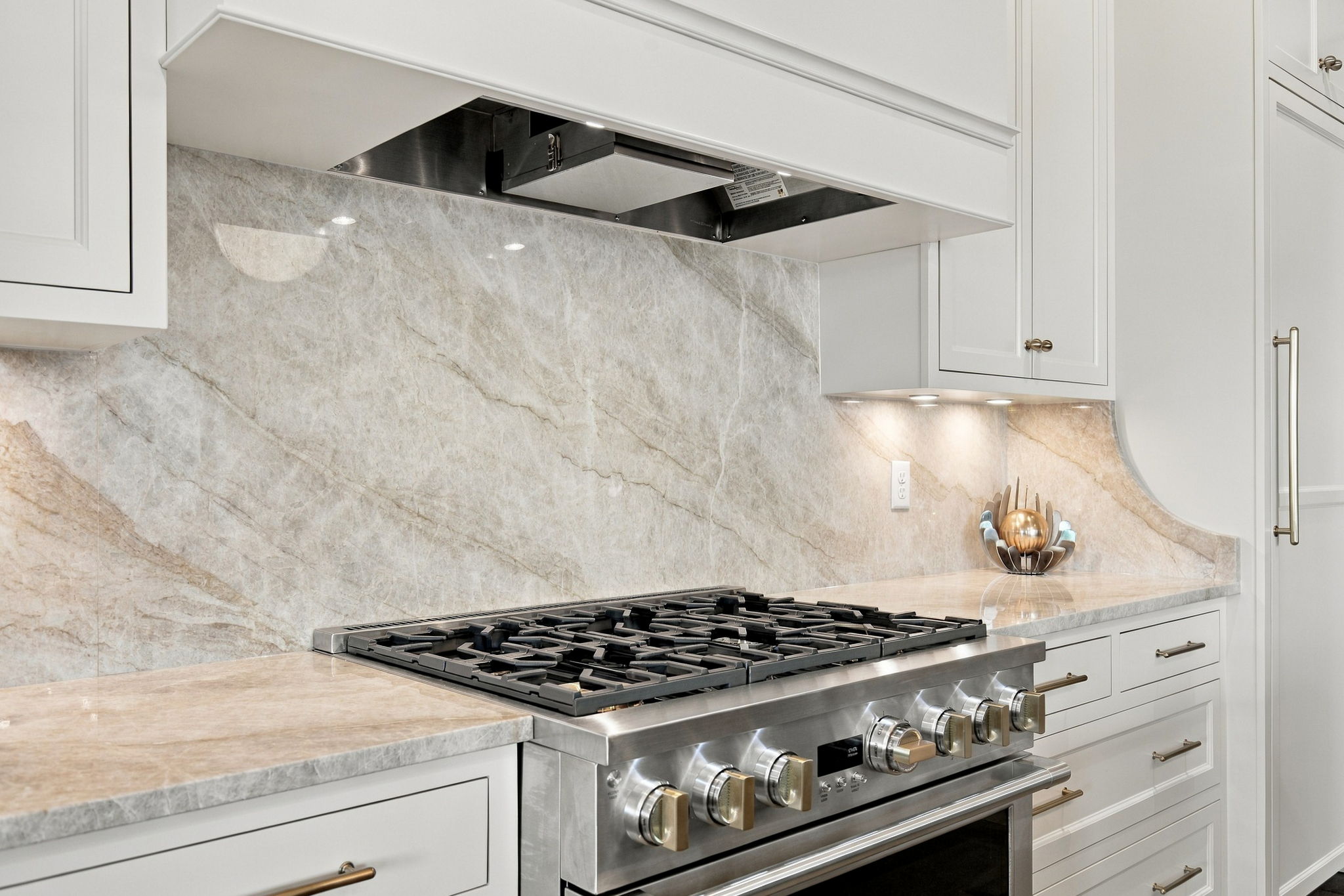 Stainless steel gas range with multiple burners, white cabinetry, and a beige marble backsplash.
