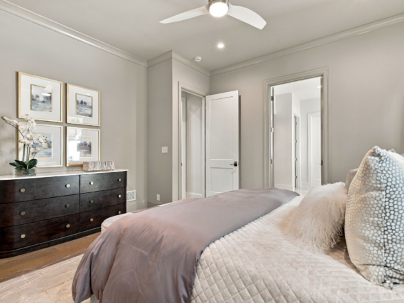 Bedroom with taupe bedding, a dark wood dresser, and four framed gold-framed artworks on a light gray wall.