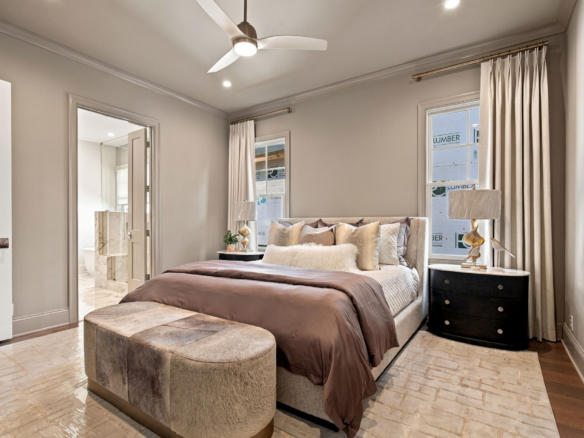 Modern bedroom with a king bed, tufted headboard, plush pillows, and matching nightstands; doorway to marble bathroom nearby