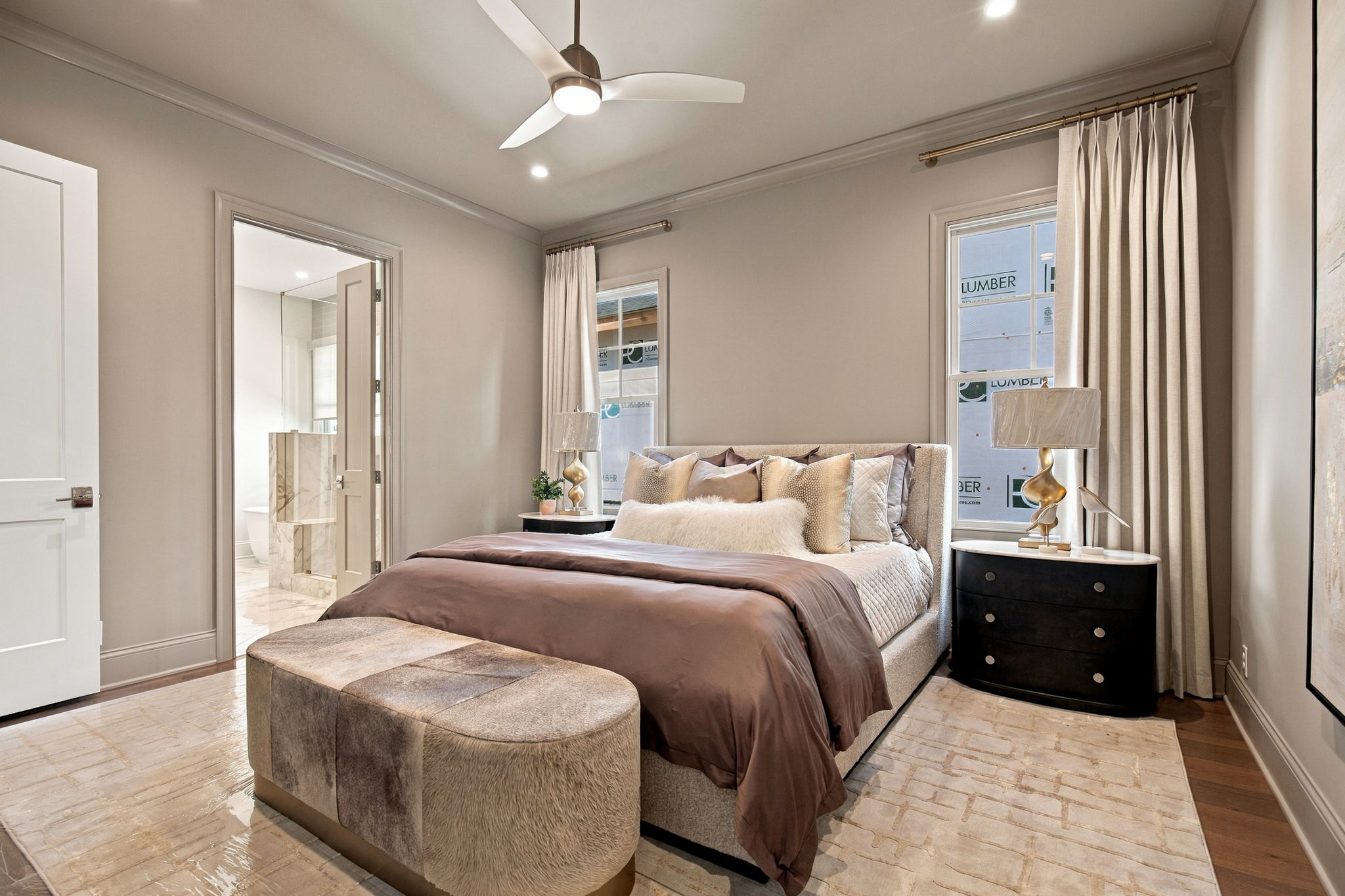 Modern bedroom with a king bed, tufted headboard, plush pillows, and matching nightstands; doorway to marble bathroom nearby