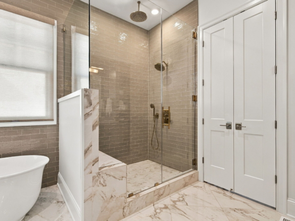 Modern glass-enclosed shower with brass fixtures, beige subway tile, and marble floor.