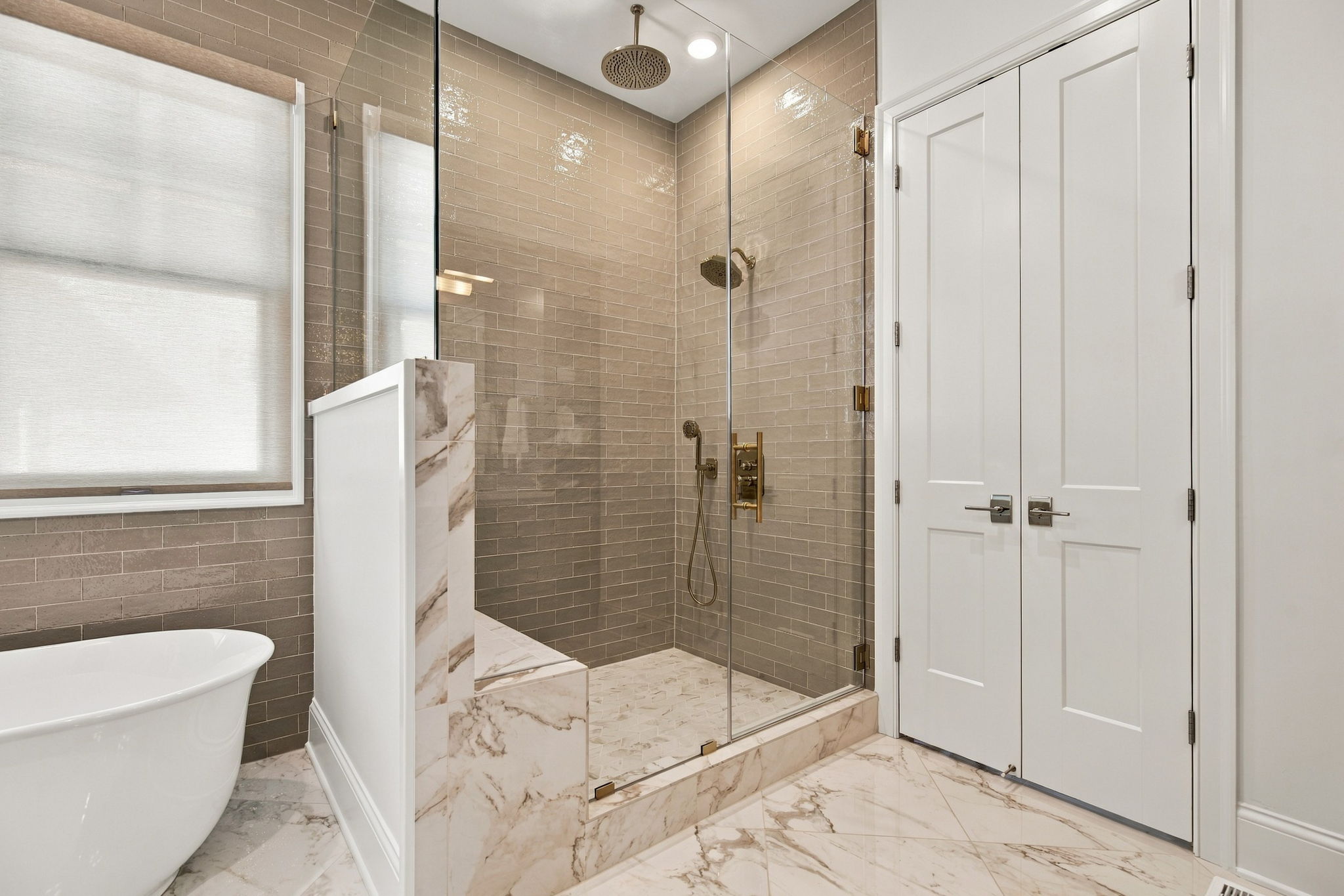 Modern glass-enclosed shower with brass fixtures, beige subway tile, and marble floor.