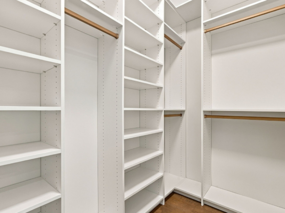 Empty white modular closet with multiple shelves and copper hanging rods for clothes