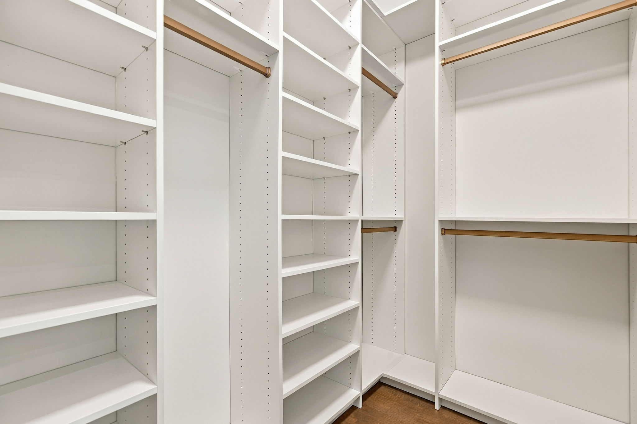 Empty white modular closet with multiple shelves and copper hanging rods for clothes