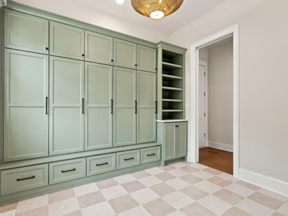 Green built-in cabinet wall with multiple doors, black hardware, and open shelving next to a doorway on the right.