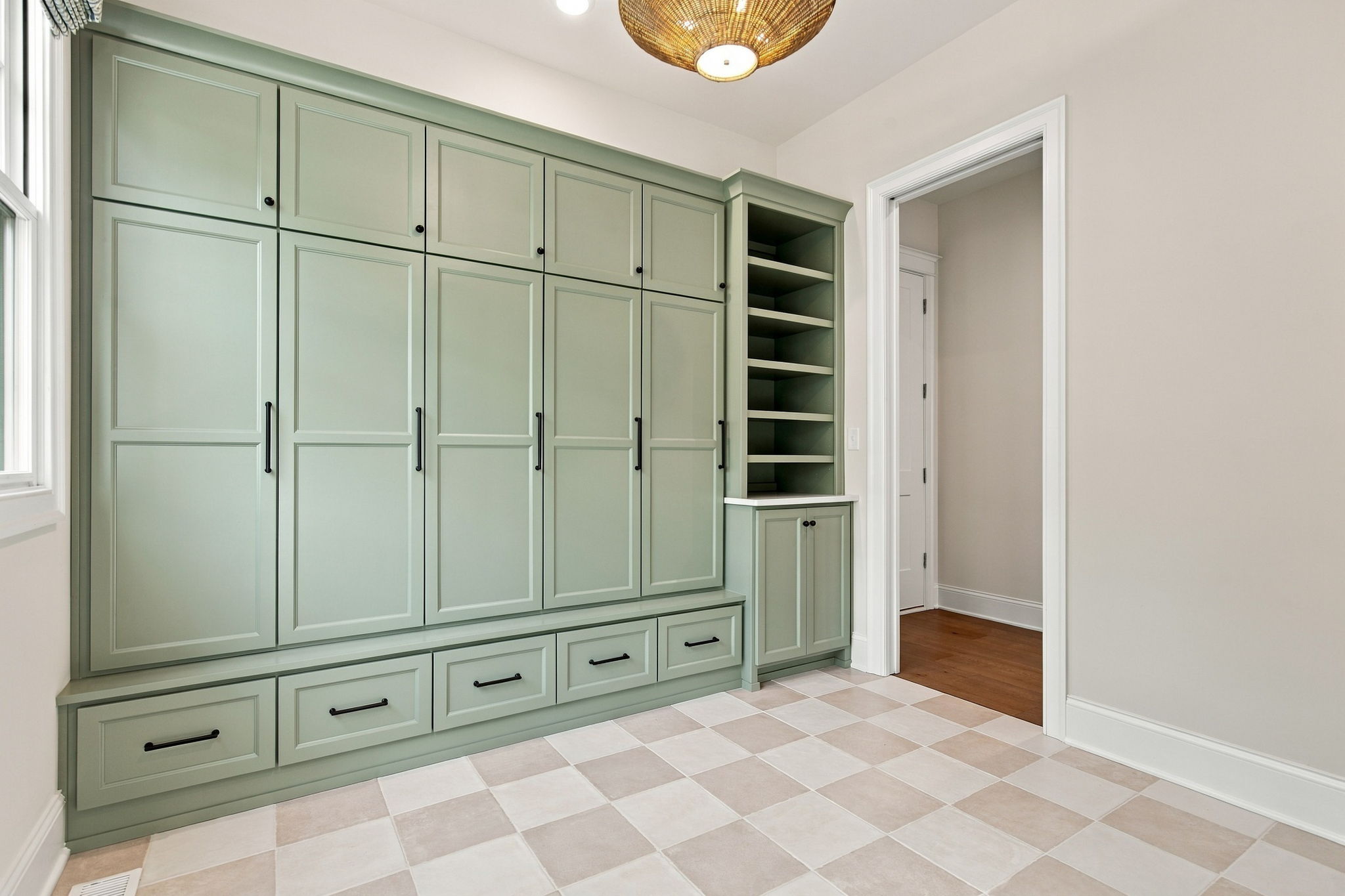 Green built-in cabinet wall with multiple doors, black hardware, and open shelving next to a doorway on the right.
