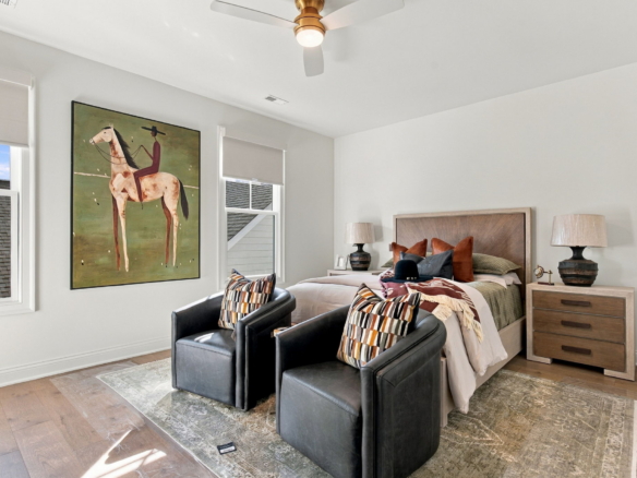 Bedroom with a large painting of a rider on a horse next to the bed and two black leather chairs in the foreground.