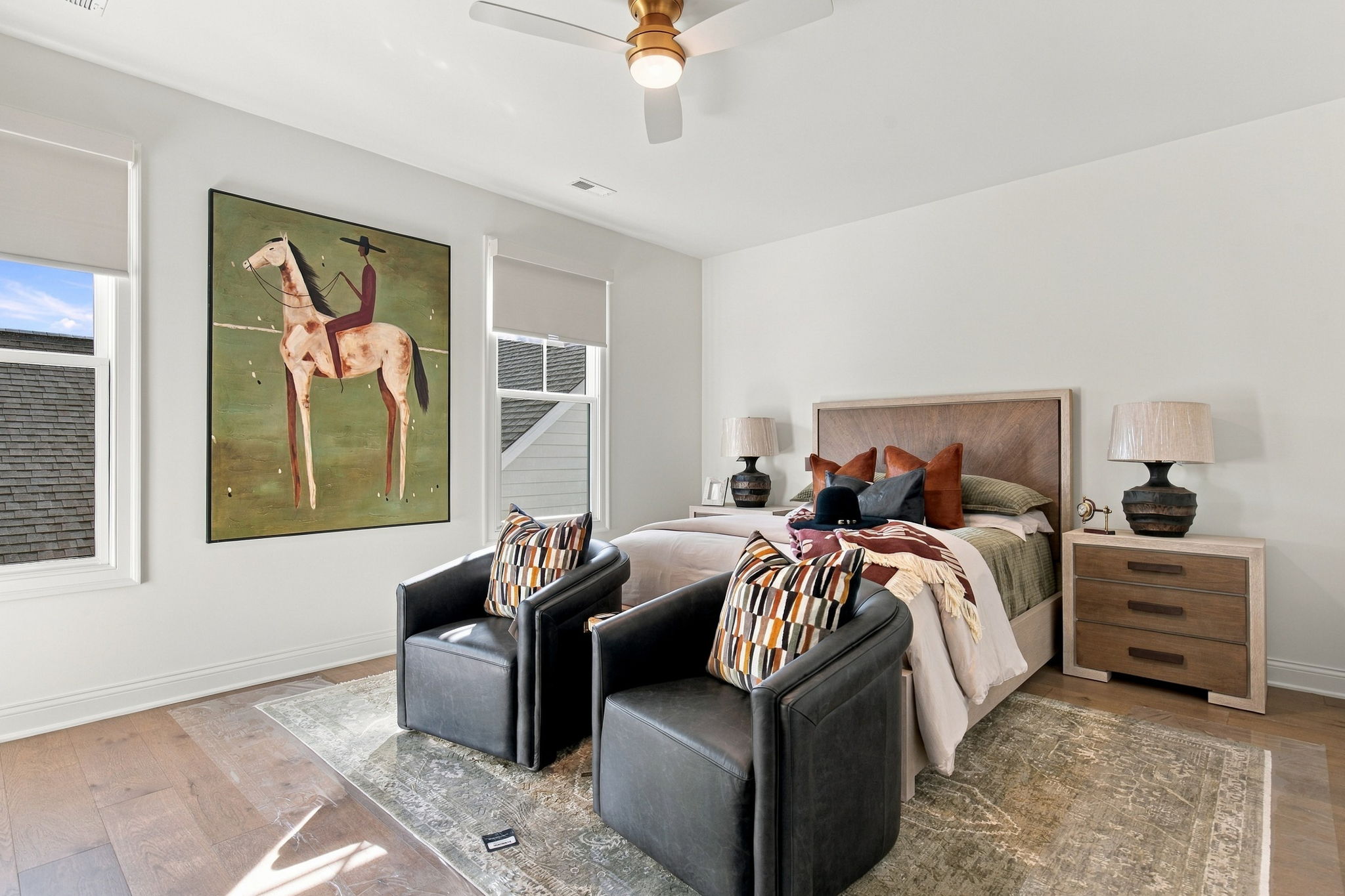 Bedroom with a large painting of a rider on a horse next to the bed and two black leather chairs in the foreground.