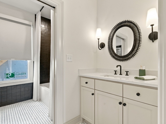 Modern bathroom with white vanity, black hardware, and a large circular woven-motif mirror flanked by two wall sconces.