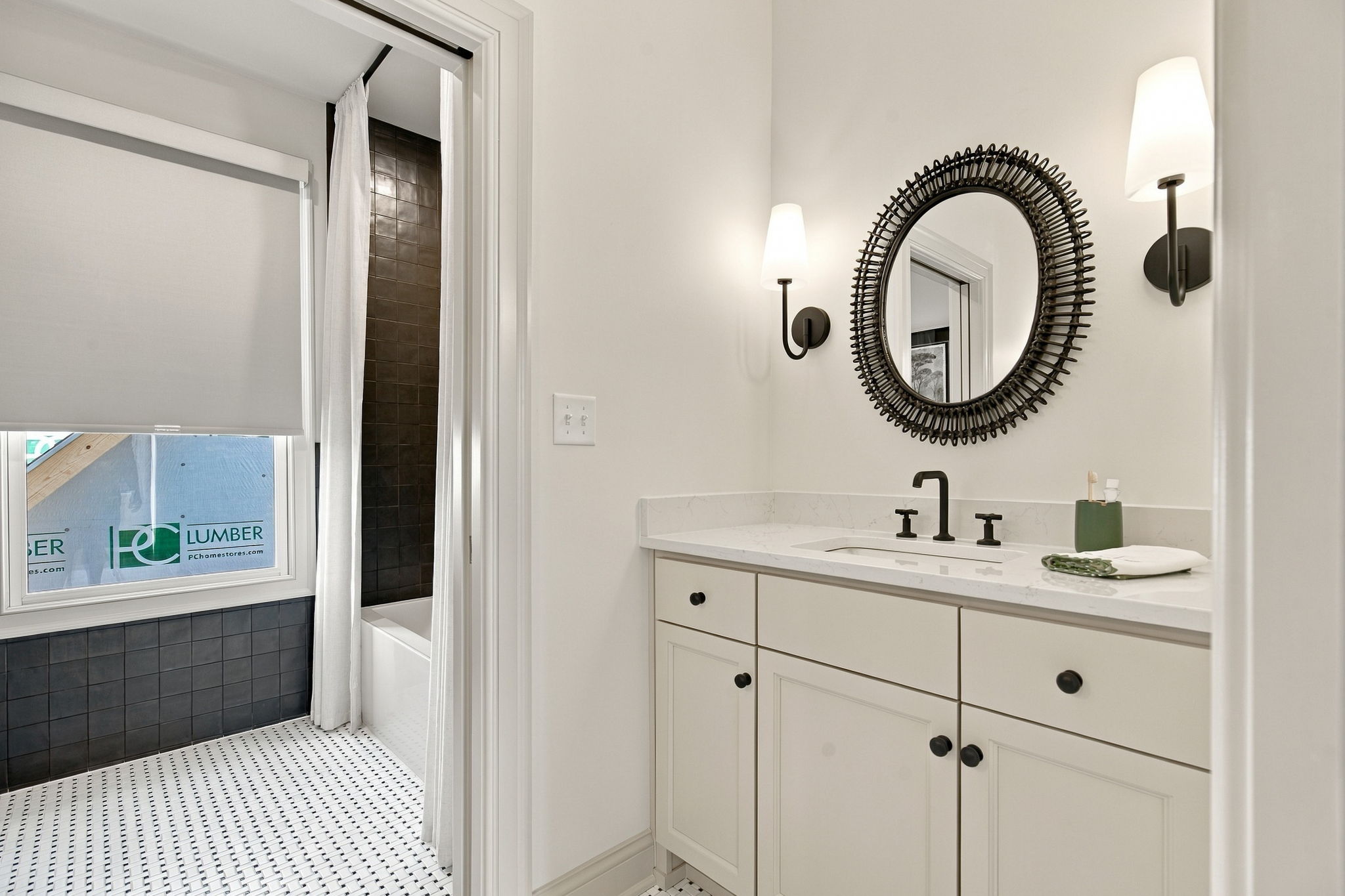 Modern bathroom with white vanity, black hardware, and a large circular woven-motif mirror flanked by two wall sconces.