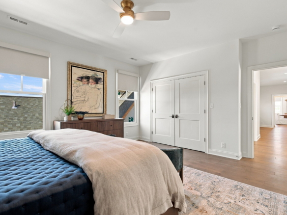 Bedroom with a navy tufted bed and beige throw, a wooden dresser, and framed artwork beneath two windows with white blinds.