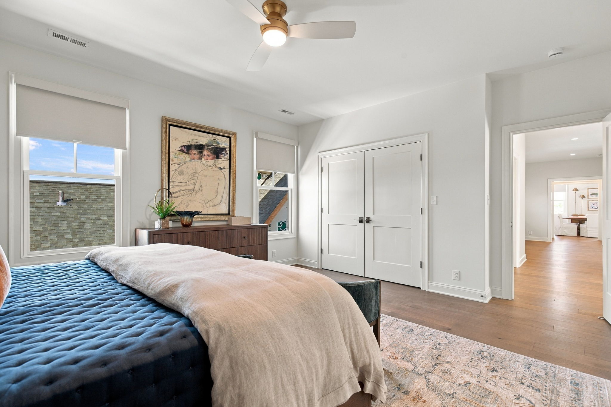 Bedroom with a navy tufted bed and beige throw, a wooden dresser, and framed artwork beneath two windows with white blinds.