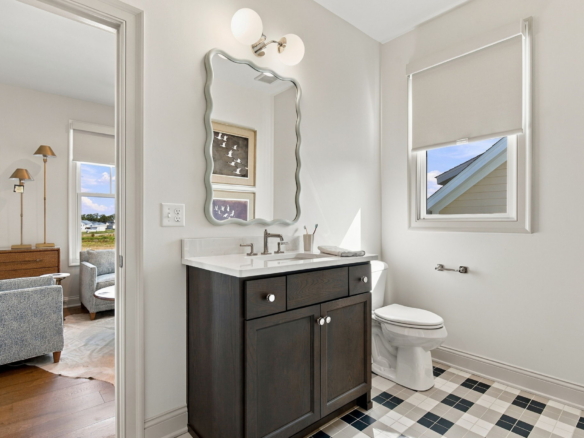 Bathroom with dark wood vanity, white countertop, wavy-edge mirror, and a two-light wall sconce above; window with blind to the right.