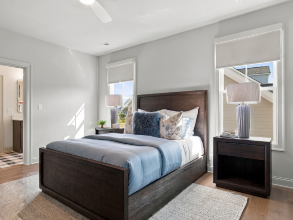 Bedroom with a dark wood bed, blue bedding, and two matching nightstands with lamps; two windows with blinds flank the bed