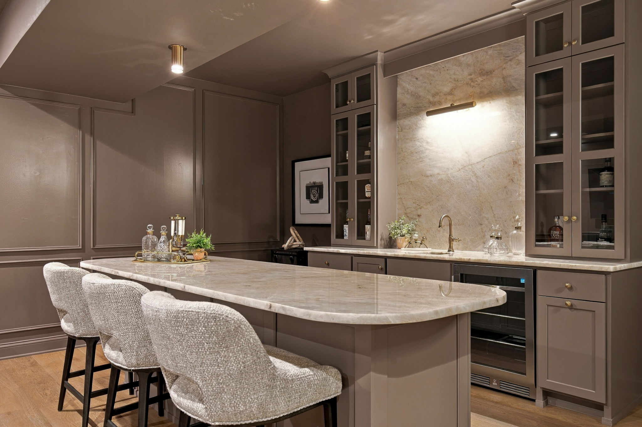 Contemporary grey kitchen with a marble island, bar seating, and glass-front cabinets.
